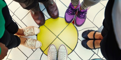 5 par fötter med skor i olika färger som står i en cirkel