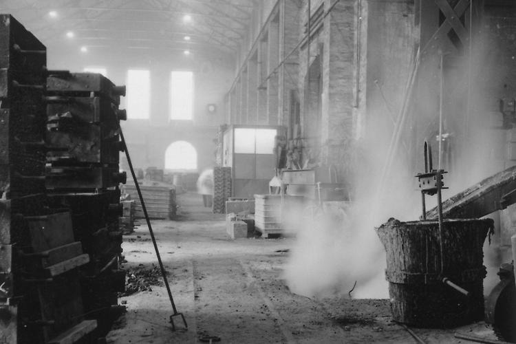 A black and white photo of a smoky factory hall. There are different machines and tools.