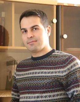 Amir Pakpour stands infront of a bookcase and looks out towards the camera.